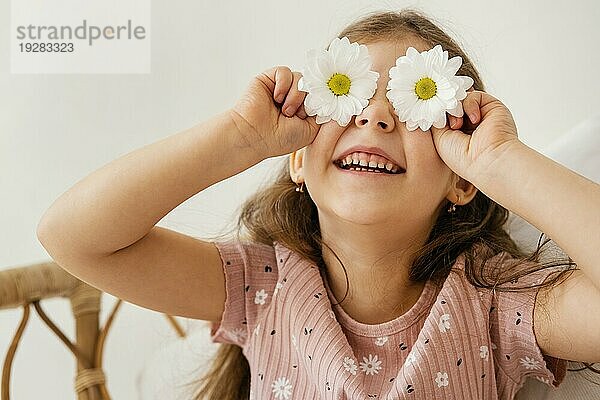 Lächelndes kleines Mädchen spielt mit Frühlingsblumen  die ihre Augen bedecken