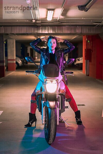 Fotografie mit blauen und rosa Neons auf einem Motorrad. Junges blondes kaukasisches Modell posiert in einer schwarzen Lederjacke