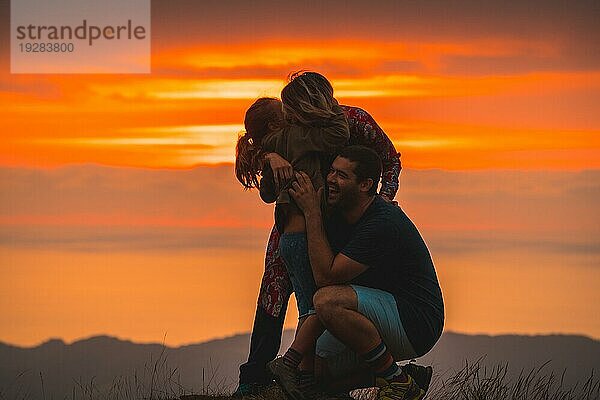 Eine Familie  die sich auf dem Gipfel eines Berges bei Sonnenuntergang umarmt und Spaß hat. Abenteuer Lebensstil Ein Sommernachmittag in den Bergen des Baskenlandes