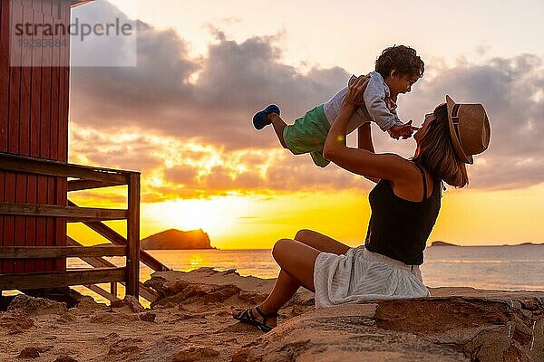 Eine Mutter vergnügt sich mit ihrem Sohn bei Sonnenuntergang am Strand von Cala Comte auf der Insel Ibiza. Balearen
