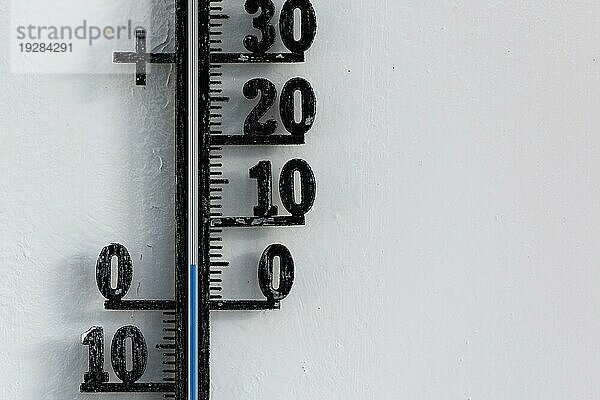 Klassisches schwarzes analoges Thermometer  das an einer weißen Wand hängt und eine blaue Temperaturskala von fünf  5 Grad Celsius anzeigt