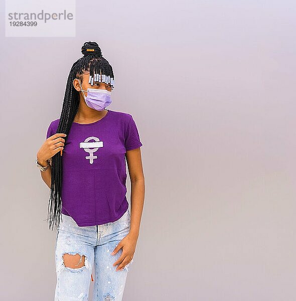 Internationaler Frauentag im Jahr der Coronaviruspandemie Covid 19. Dominikanische Frau mit feministischem lila Hemd und Gesichtsmaske