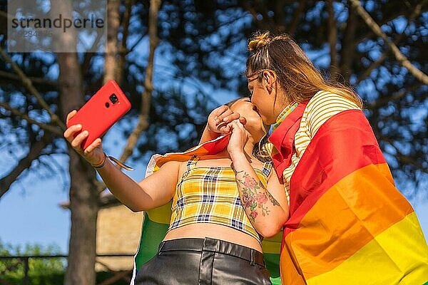 Eine Nahaufnahme von zwei jungen kaukasischen umarmen Frauen mit LGBT Stolz Flagge unter Selfie im Freien