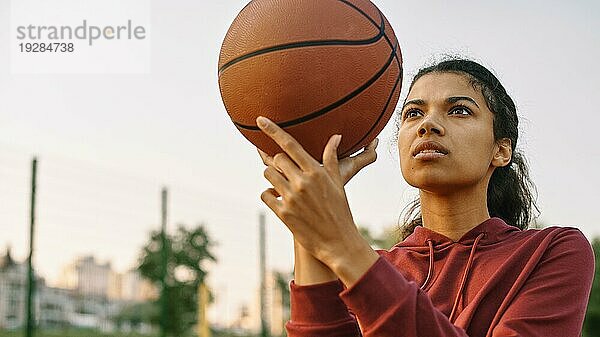 Junge Frau spielt draußen Basketball