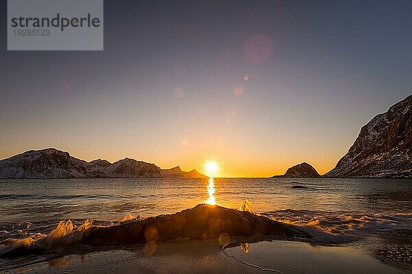 Der berühmte Sandstrand bei Haukland während des Sonnenuntergangs auf den Lofoten in Norwegen an einem klaren Wintertag mit schneebedeckten Bergen und blauem Himmel