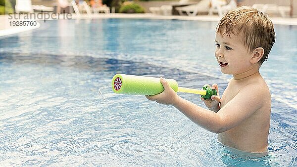 Junge spielt mit Wasserpistole im Pool