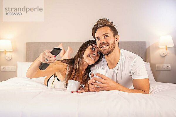 Ein verliebtes Paar  das auf dem Hotelbett im Schlafanzug fernsieht  Lebensstil eines liebenden Paares