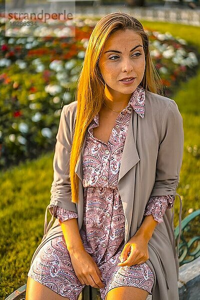 Lifestyle  ein junger Unternehmer. Kaukasierin und Blondine mit kastanienbraunem Regenmantel und Blumenkleid in der Stadt. Luftaufnahme neben den Blumen in einem schönen Park  junge Frau schaut nach rechts