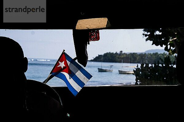 Innenaufnahme eines Autos mit kubanischer Flagge  das auf das Meer zufährt