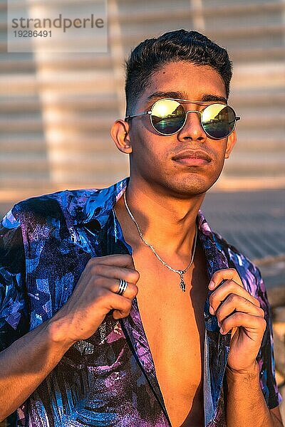 Sommerlicher Lebensstil  ein junger Latino genießt die Sommerferien. mit lila Blumenhemd und Sonnenbrille  beobachtet den Sonnenuntergang
