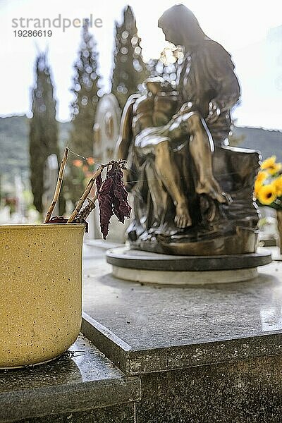 Blumentopf mit verwelkter Blume auf einem Grab vor einer religiösen Marienfigur mit Jesus in den Armen im Gegenlicht  Bari Sardo  Ogliastra  Sardinien  Italien  Europa