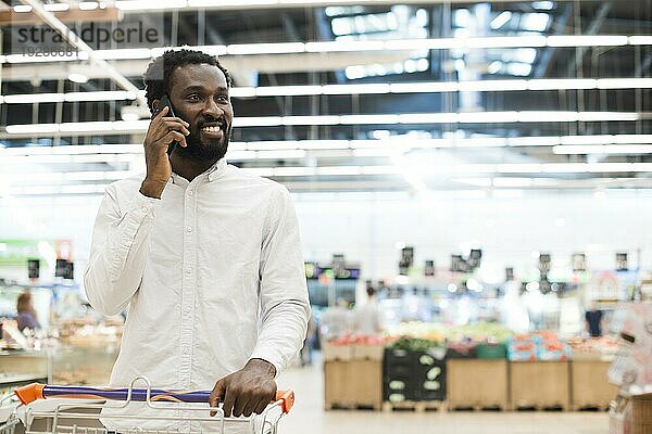 Fröhlicher schwarzer Mann  der mit einem Mobiltelefon Lebensmittel verkauft