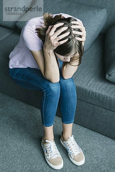 Junge Frau mit Kopfschmerzen auf dem Sofa sitzend