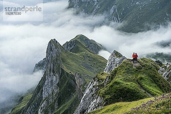 Zwei Wanderer genießen Ausblick über Säntis Gebirge ins Tal der Meglisalp bei Sonnenaufgang  Hochnebel im Tal  Säntis  Appenzell Ausserrhoden  Appenzeller Alpen  Schweiz  Europa