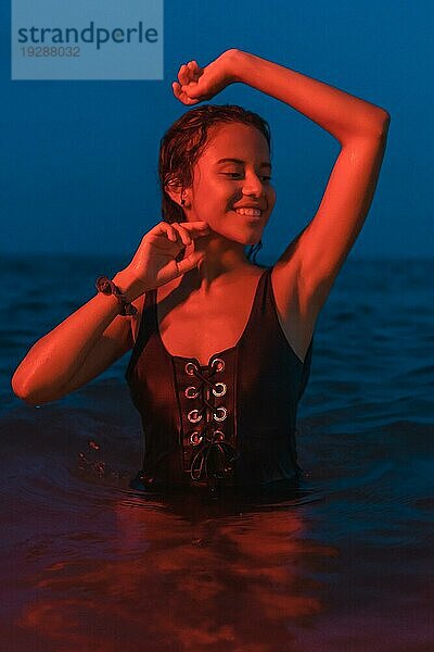 Lifestyle einer jungen hübschen brünetten Kaukasierin beim nächtlichen Baden im Meer mit einem beleuchteten roten Licht  vertikales Foto
