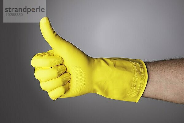 Eine Hand mit gelbem Schutzhandschuh macht ein Daumen hoch Zeichen