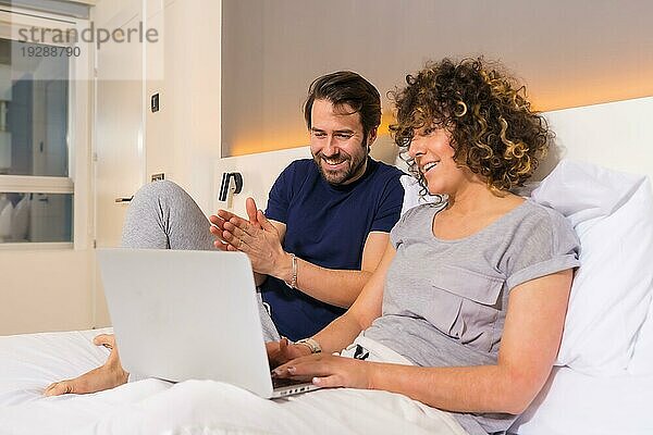 Lifestyle  ein Paar im Schlafanzug auf dem Bett  das eine Online Reservierung auf dem Computer betrachtet