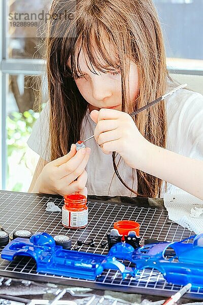 Ein Kleinkind bemalt zu Hause ein Plastikmodell eines Spielzeugautos