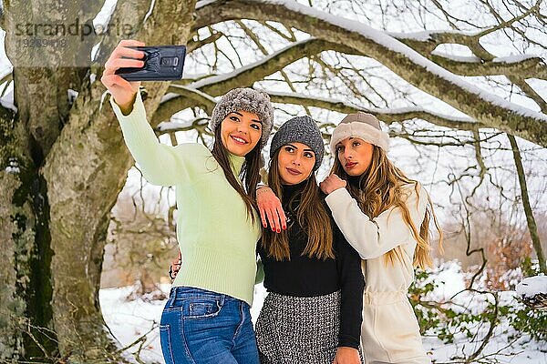 Winter Lifestyle  drei schöne kaukasische Freunde nehmen ein Selfie mit dem Telefon im Schnee unter einem Baum  Urlaub in der Natur