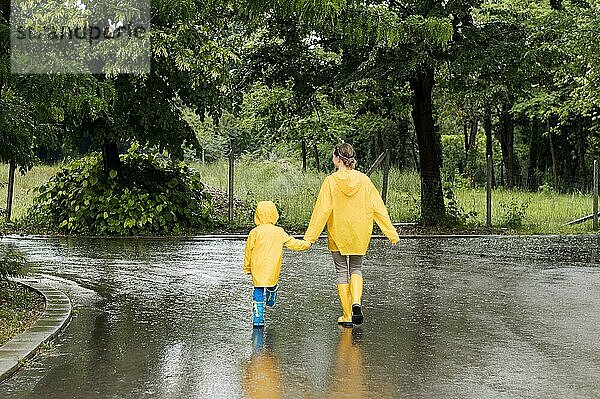 Langer Schuss Mutter Sohn hält Hände  während tragen regen Mäntel