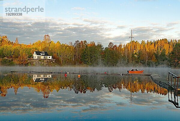 Boot  Bäume und Häuser spiegeln sich an einem ruhigen Herbstmorgen im Wasser des Bullaren  See  Oktober  Bohuslän  Schweden  Europa