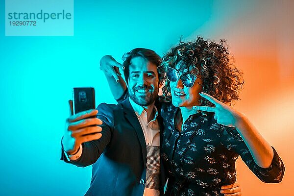 Party Lifestyle  ein verliebtes kaukasisches Paar macht ein Selfie auf einer Party mit orangefarbenen und blauen Lichtern  am Valentinstag