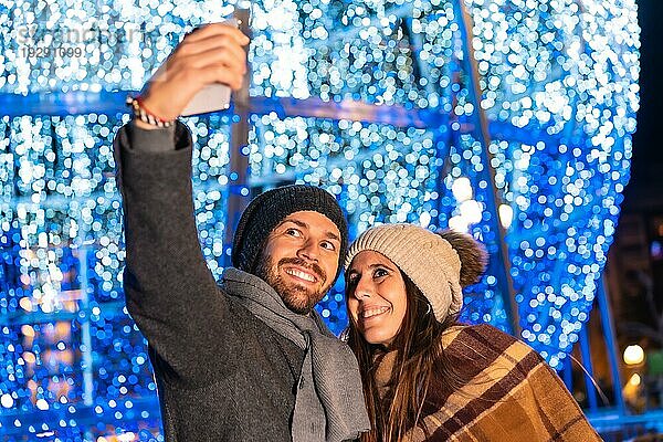 Ein junges europäisches Paar  das die Weihnachtsbeleuchtung der Stadt genießt und ein Selfie mit dem Handy für soziale Netzwerke macht  Lifestyle