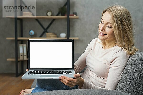 Glückliche junge Frau hält ihren geöffneten Laptop mit weißem Bildschirm in der Hand