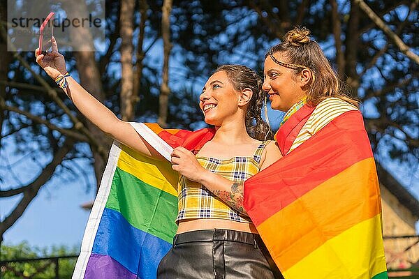 Eine Nahaufnahme von zwei jungen kaukasischen umarmen Frauen mit LGBT Stolz Flagge unter Selfie im Freien
