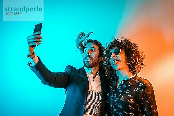 Party Lifestyle  ein kaukasisches Paar macht ein Selfie auf einer Party mit orangen und blauen Lichtern