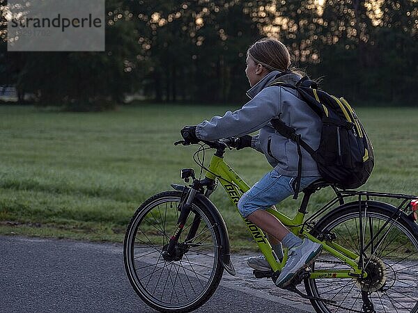 Kind  Junge fährt mit Fahrrad und Schultasche am Morgen am Wiesenrand