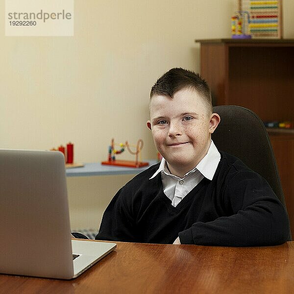 Junge mit Down Syndrom posiert mit Laptop