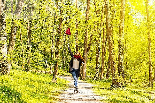 Lateinamerikanisches Mädchen mit schwarzer Jacke  Schal und roter Wollmütze in einem herbstlichen Park  das den Hut wirft  während es fröhlich spazieren geht