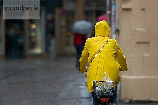 Eine unerkennbare Person mit gelbem Ölzeug auf dem Fahrrad  die durch eine verregnete Straße in einer alten  engen Schusterstraße mit Kopfsteinpflaster fährt