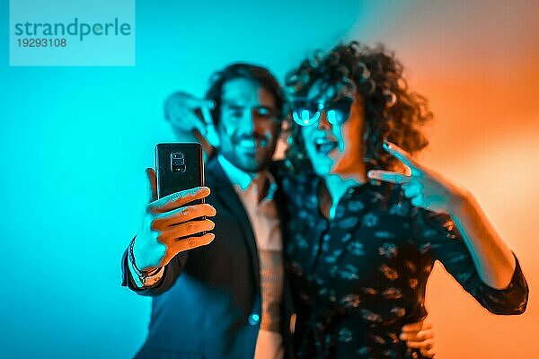 Party Lifestyle  ein verliebtes kaukasisches Paar macht ein Selfie auf einer Party mit orangen und blauen Lichtern