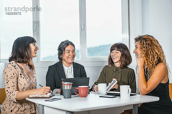 Sitzung junger Unternehmer im Büro  ein junger Mann lateinamerikanischer Herkunft und drei junge kaukasische Frauen  die an einem Sommermorgen an einem Tisch im Büro sitzen