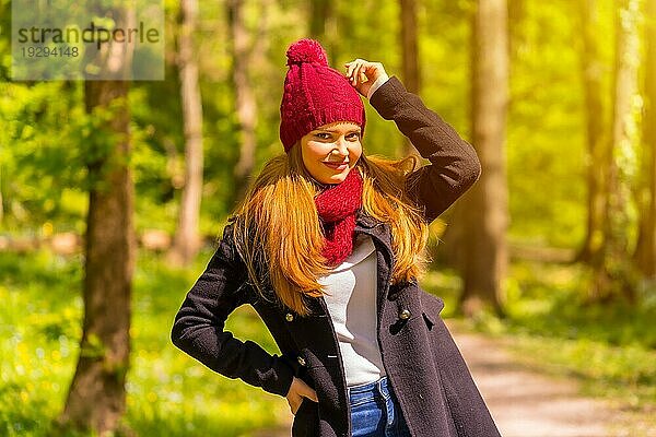 Lateinamerikanisches Mädchen mit schwarzer Jacke  Schal und roter Wollmütze in einem herbstlichen Park  lächelnd in die Kamera schauend