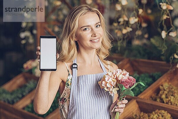 Lächelndes Porträt blonde junge Frau hält Blumenstrauß Hand zeigt Handy