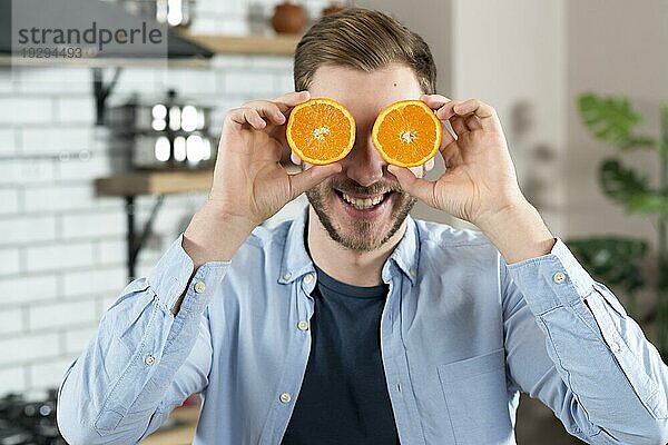 Junger Mann macht sich einen Spaß mit zwei Orangenscheiben zu Hause