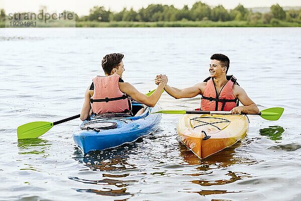 Zwei männliche Freunde schütteln einander die Hand beim Kajakfahren auf dem See