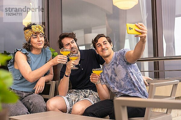 Freunde machen ein Selfie und gratulieren sich mit Cocktails auf der Terrasse einer Bar