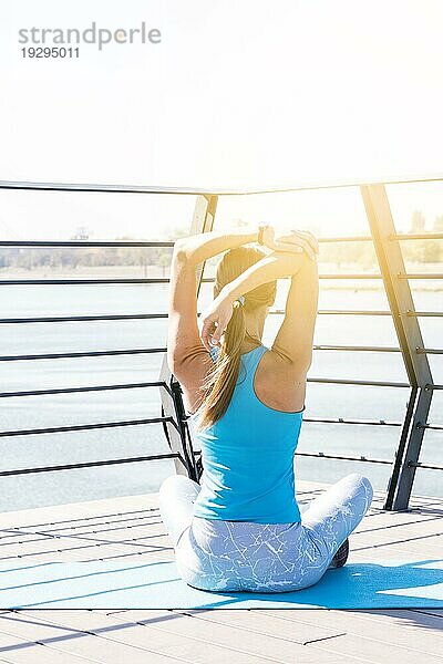 Rückansicht junge Fitness Frau streckt ihre Hand sitzen Brücke Morgensonne