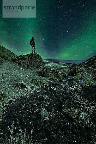 Die Silhouette eines jungen Mädchens in einer Nacht mit wunderschönen Nordlichtern. Island