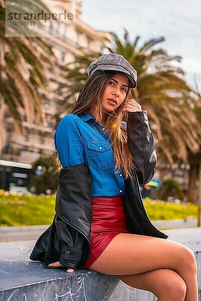 Street Style in der Stadt  eine hübsche brünette Kaukasierin in einem Jeanshemd  einer Baskenmütze und einem kurzen roten Rock genießt die Sommerferien