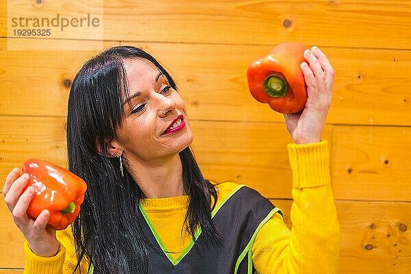 Ein brünettes kaukasisches Obstmädchen  das in einem Gemüseladen arbeitet  hat Spaß an roten Paprika in der Hand