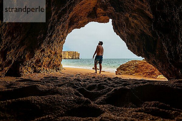 Ein Mann in einer natürlichen Höhle an der Algarve im Sommer am Strand von Praia da Coelha  Albufeira. Portugal