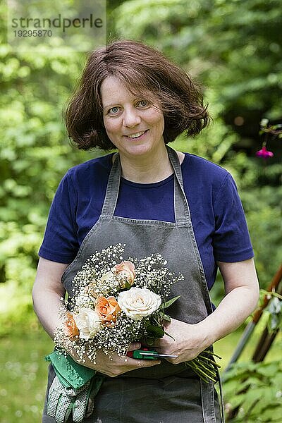 Gärtnerin mit Blumenstrauß und Schürze im Garten  gardener with bouquet of flowers and apron in a garden