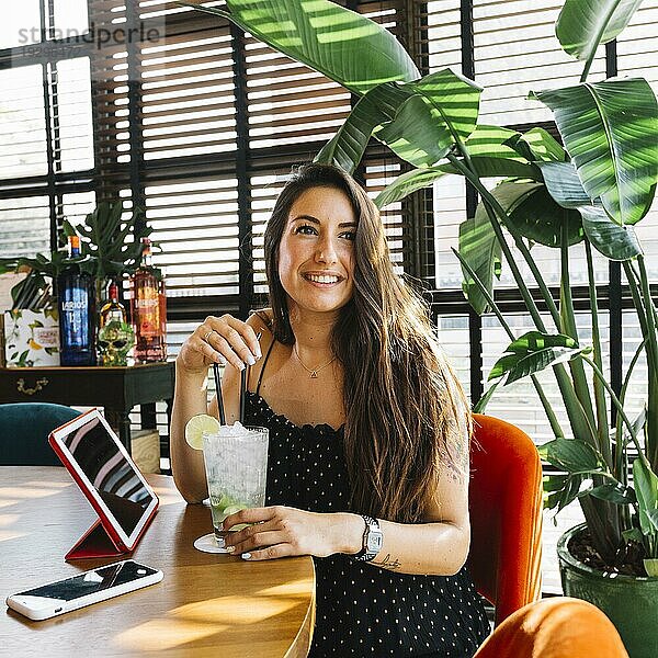 Lächelnde schöne junge Frau mit Cocktail Smartphone digitale Tablette Restaurant