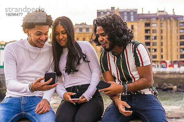 Lifestyle  drei schwarze Freunde  die Spaß haben und soziale Medien auf der Straße beobachten. Afro Haar Junge  Brünette Junge mit langen Haaren und Brünette Mädchen