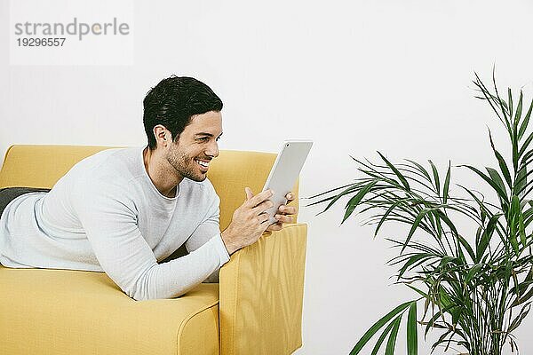 Glücklicher junger Mann auf dem Sofa mit Tablet